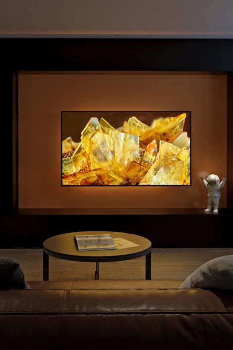 home theater with a large screen displaying a close-up of yellow crystals, a small astronaut figurine on the right, and a round table with magazines in front of a leather couch.